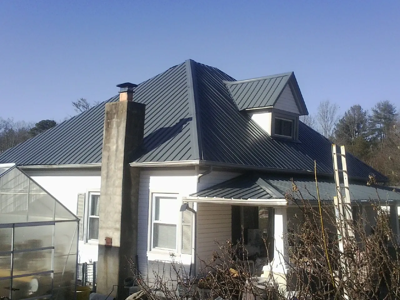 Dark blue standing seam metal roof on a white farmhouse with dormer — Slate & Tile Roof Repair by Roofing Brothers in Casnovia
