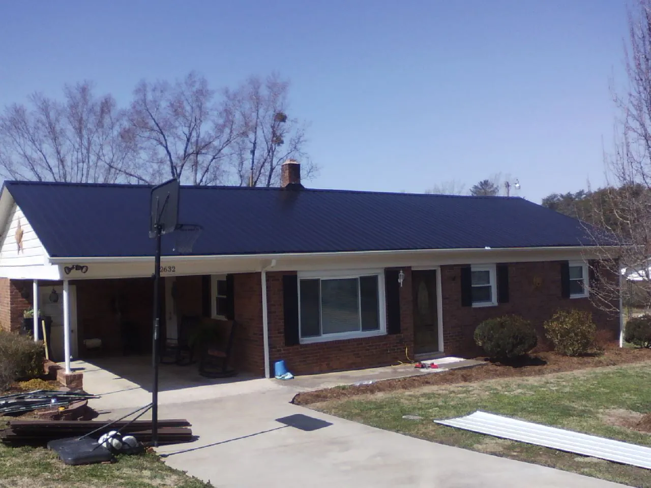 Finished dark blue metal roof on a brick ranch with a carport in Casnovia