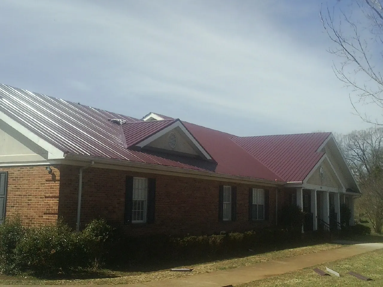 Red metal roof with gabled entries on a long brick building, from a Hail Damage Roof Repair job in Casnovia