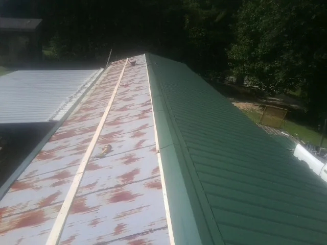 Old rusted panels beside newly installed green metal roofing — Wind Damage Roof Repair by Roofing Brothers in Casnovia