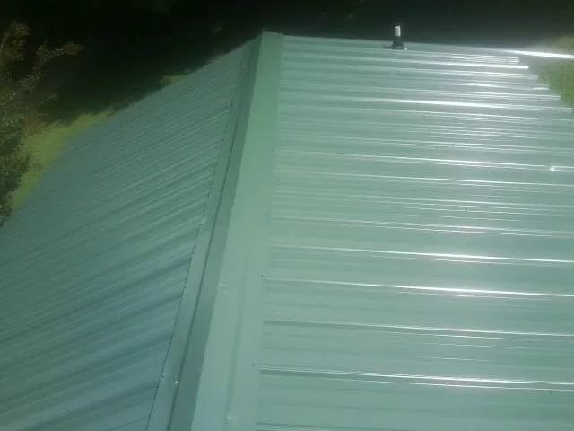 New green metal panels meeting at the ridge of a roof — Flat Roof Repair work by our crew in Casnovia