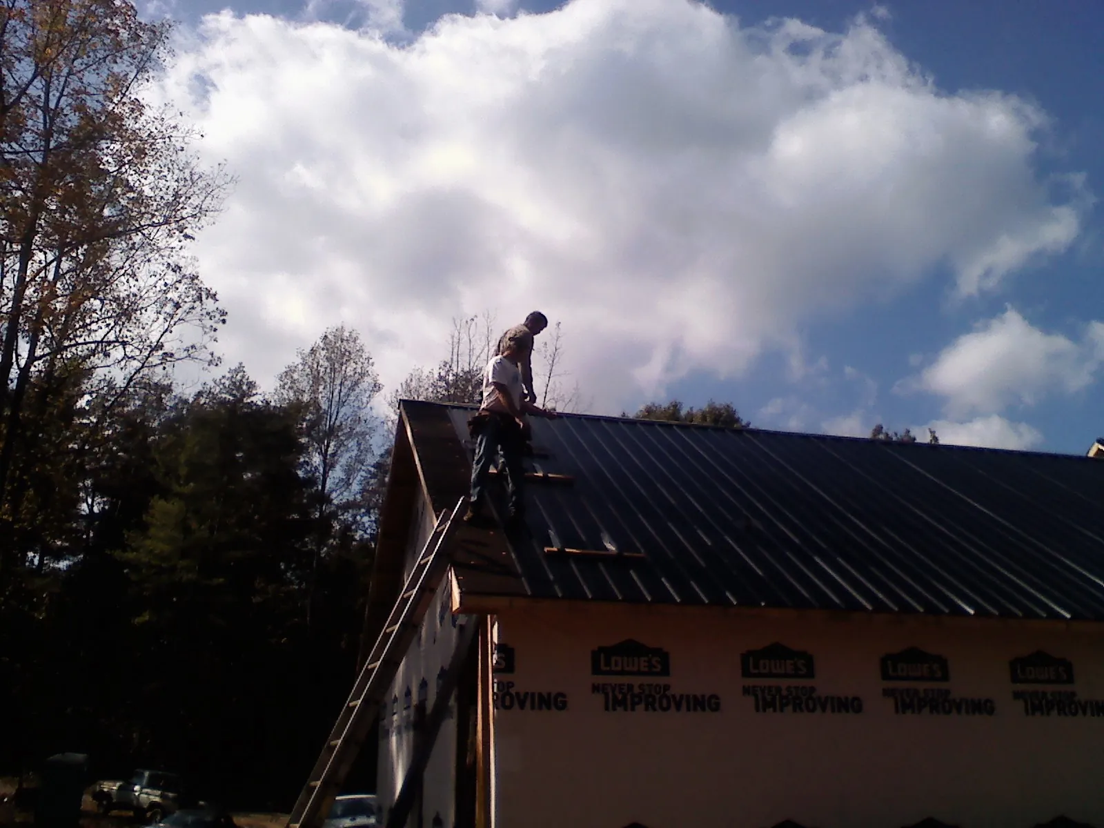 Roofer fastening dark metal panels high against a cloudy sky, from a Roof Inspection job in Casnovia