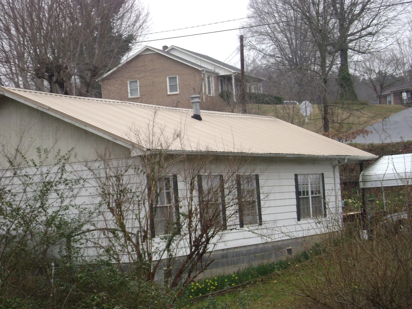 Tan metal roof on a white sided house set into a hillside — Commercial Roofing by Roofing Brothers in Casnovia