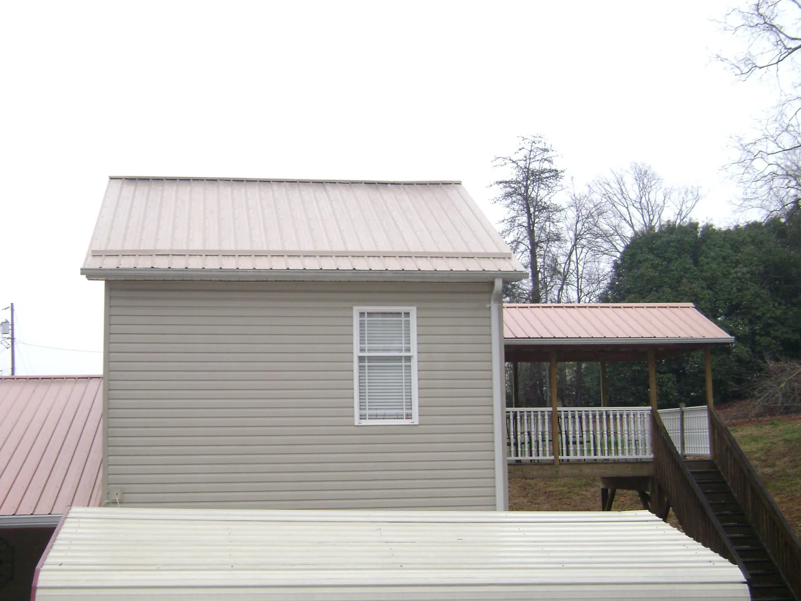 Tan metal roofs on a two story addition and attached porch, from a Roof Replacement job in Casnovia